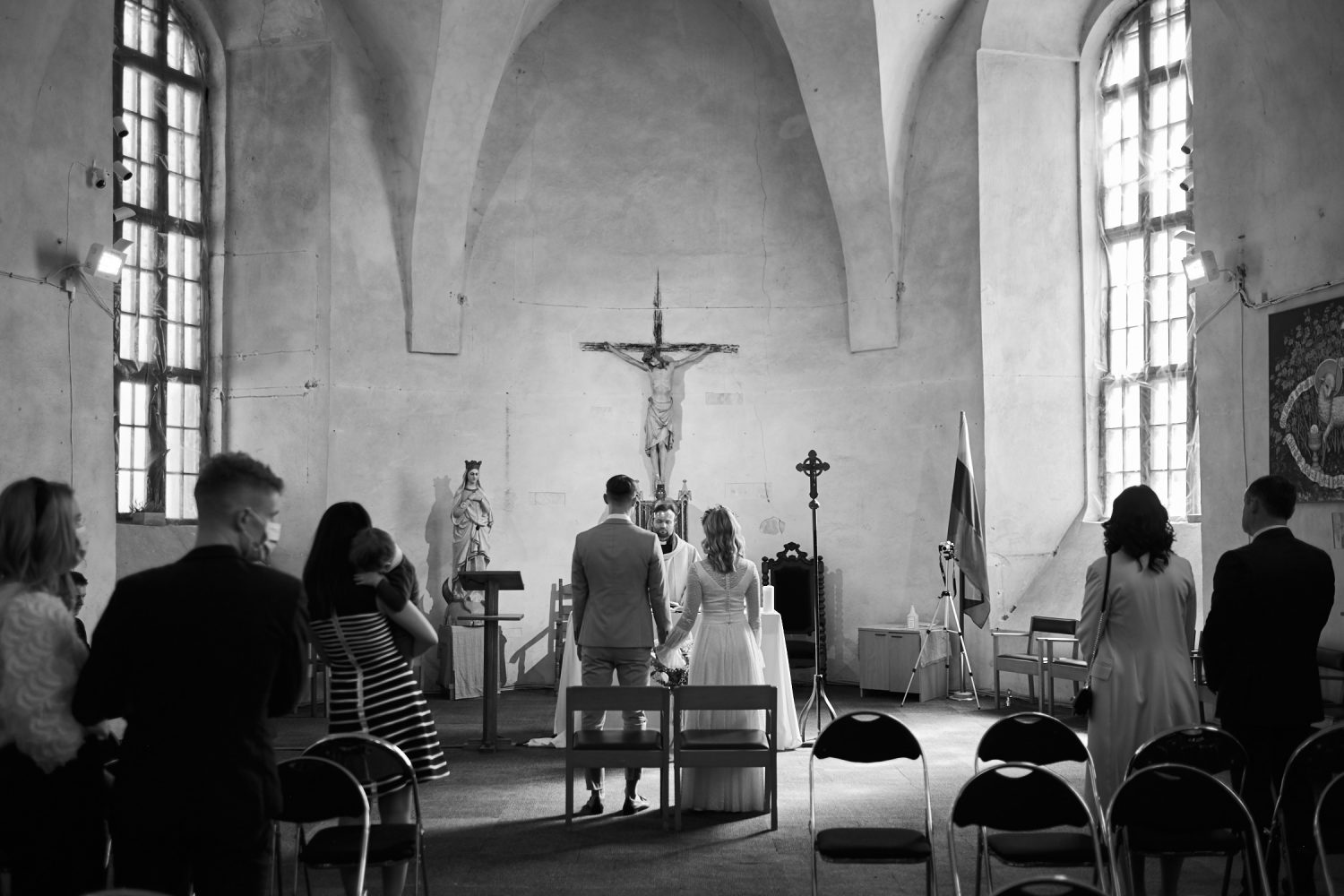 Ceremonija bažnyčioje, Milda ir Vilius stovi altoriaus fone, bendro plano juodai balta nuotrauka